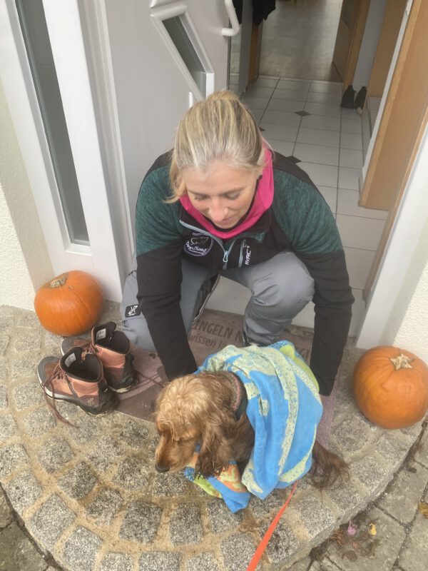 Hundetrainerin Evelien Smit trocknet einen glücklichen Besuchshund nach einem langen Spaziergang in der Hundepension DogBones in Bodnegg